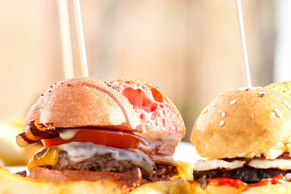 Dos Hamburguesas con carne queso tomate y beicon. El pan de arriba de la hamburguesa de la izquierda tiene un color distinto al normal , con una tonalidad rosada.